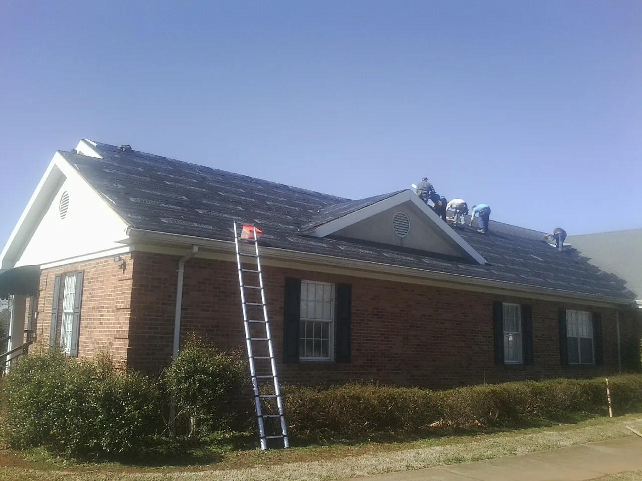Crew tearing shingles off a brick ranch roof with a ladder set — Metal Roof Repair work by our crew in Franklinville