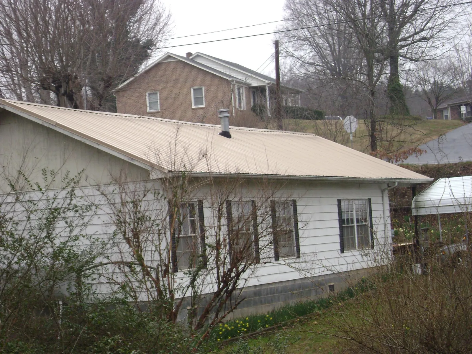 Tan metal roof on a white sided house set into a hillside — Commercial Roofing by Roofing Brothers in Franklinville