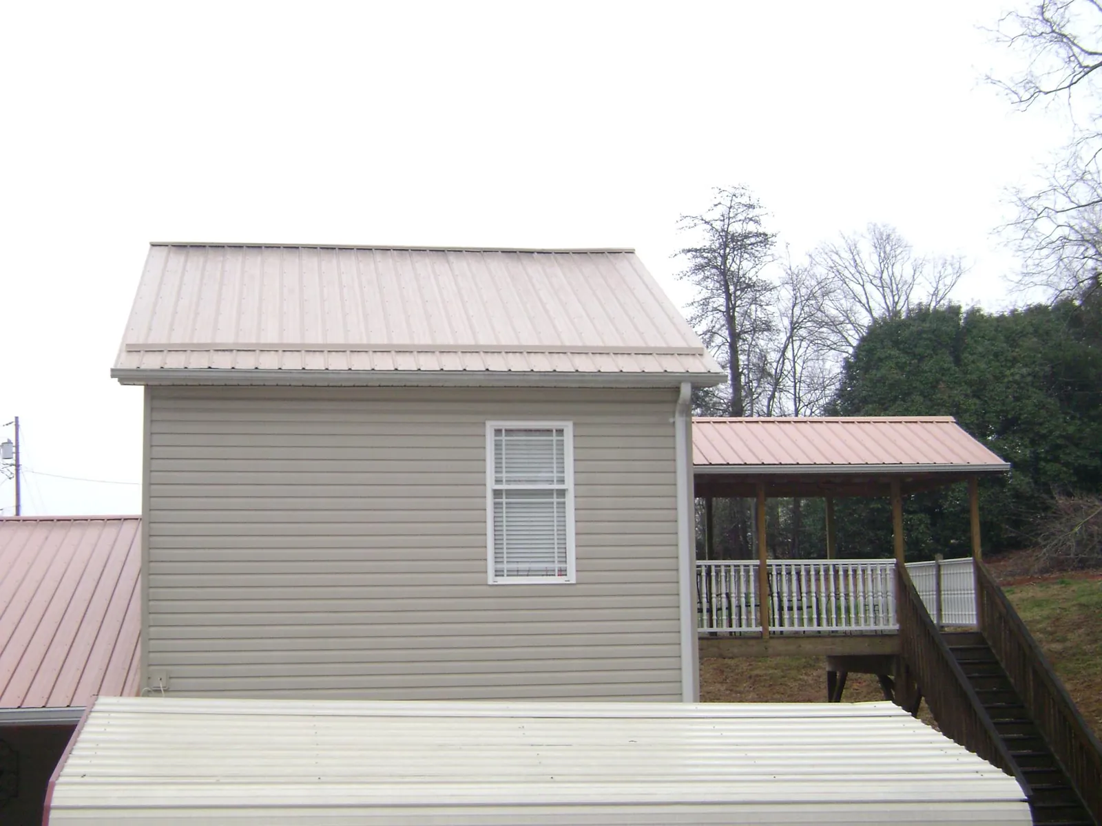 Tan metal roofs on a two story addition and attached porch, from a Roof Replacement job in Franklinville